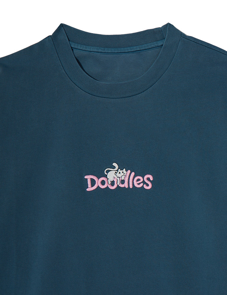 Slate crewneck t-shirt featuring an embroidered Mello design lounging atop the Doodles logo, inspired by Dullsville and The Doodleverse. Logo close-up.